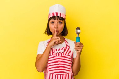 Genç melez dondurma üreticisi kadın sarı arka planda izole edilmiş dondurma tutuyor. Genç melez dondurma üreticisi kadın sarı arka planda izole edilmiş dondurma kepçesini tutuyor ya da bir sır saklıyor ya da sessizlik istiyor..