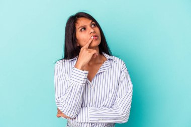 Mavi arka planda izole edilmiş genç Latin kadın şüpheli ve şüpheci bir ifadeyle yana bakıyor..