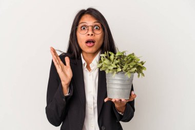 Beyaz arka planda bitkileri tutan genç Latin kadın şaşırdı ve şok oldu..