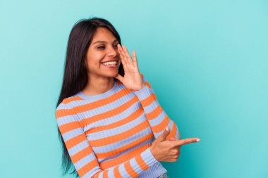 Genç Latin bir kadın mavi arka planda izole edilmiş. Dedikodu yapıyor, bir şeyleri bildiriyor..