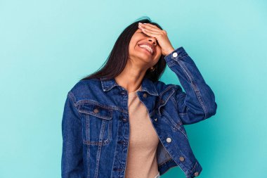 Mavi arka planda izole edilmiş genç Latin kadın ellerini başının üstünde tutarak neşe içinde gülüyor. Mutluluk kavramı.