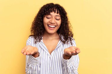 Sarı arka planda izole edilmiş genç bir ırk kadını elinde avuç içi bir şeyle kameraya sunuyor..