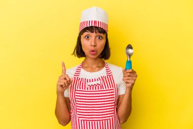 Genç melez dondurma üreticisi kadın elinde sarı arka planda izole edilmiş bir dondurma tutuyor. Genç melez dondurma üreticisi kadın sarı arka planda izole edilmiş bir dondurma kepçesi tutuyor. Harika bir fikir, yaratıcılık kavramı var..