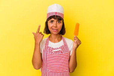 Sarı arka planda izole edilmiş dondurma tutan genç melez dondurma üreticisi kadın işaret parmağıyla yaptığı hayal kırıklığı jestini gösteriyor..