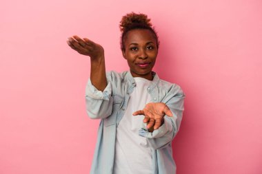 Pembe arka planda izole edilmiş genç Afrikalı Amerikalı kadın kollarıyla ölçek oluşturuyor, mutlu ve kendinden emin hissediyor..