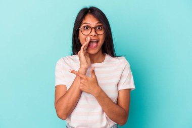 Genç Latin bir kadın mavi arka planda izole edilmiş. Dedikodu yapıyor, bir şeyleri bildiriyor..