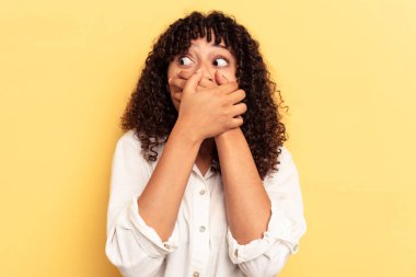 Genç melez kadın sarı arka planda izole edilmiş. Düşünceli bir şekilde bir fotokopi odasına bakıyor. Ağzını eliyle kapatıyor..