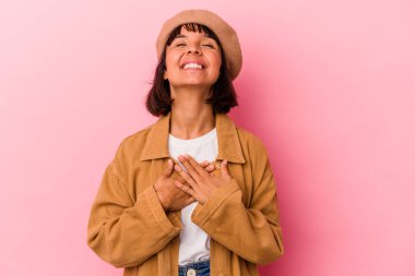 Pembe arka planda soyutlanmış genç bir ırk kadını yüksek sesle gülüyor elini göğsünde tutuyor..