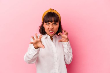 Pembe arka planda izole edilmiş genç melez kadın pençelerini kedi taklidi yaparken gösteriyor, agresif bir hareket..