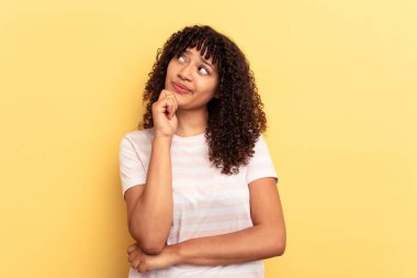 Genç melez kadın sarı arka planda izole edilmiş düşünüyor, bakıyor, yansıtıyor, düşünüyor, hayal kuruyor..