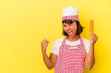 Genç melez dondurma üreticisi kadın dondurma tutuyor sarı arka planda izole edilmiş zafer kazandıktan sonra yumruk kaldırıyor, kazanan konsept..