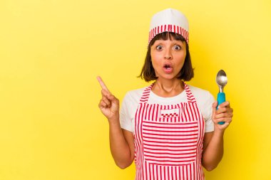 Genç melez dondurma üreticisi kadın, sarı arka planda izole edilmiş dondurma tutuyor. Küçük melez dondurma üreticisi kadın, sarı arka planda izole edilmiş bir dondurma kepçesi tutuyor.