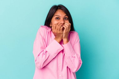 Mavi arka planda izole edilmiş, tırnak yiyen, gergin ve endişeli genç bir Latin kadın..