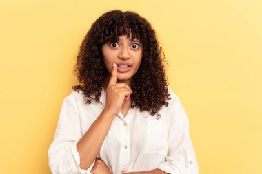 Sarı arka planda izole edilmiş genç melez kadın şüpheli ve şüpheci bir ifadeyle yana bakıyor..