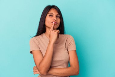 Mavi arka planda izole edilmiş genç Latin kadın alaycı bir ifadeyle kameraya bakıyor..