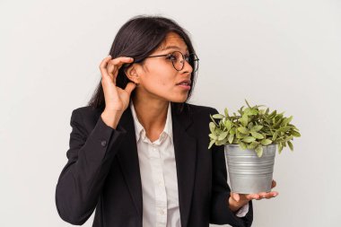 Beyaz arka planda bitkileri tutan genç Latin kadın bir dedikoduyu dinlemeye çalışıyor..