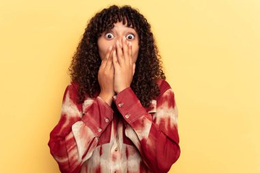 Sarı arka planda izole edilmiş genç bir ırk kadını elleriyle ağzını kapatırken şok oldu..
