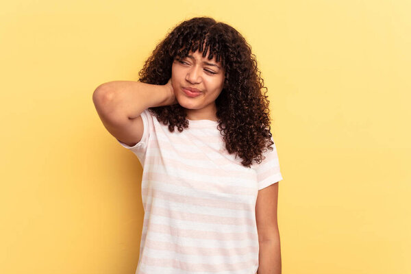 Молодая женщина смешанной расы изолирована на желтом фоне, испытывая боль в шее из-за стресса, массируя и прикасаясь к ней рукой.