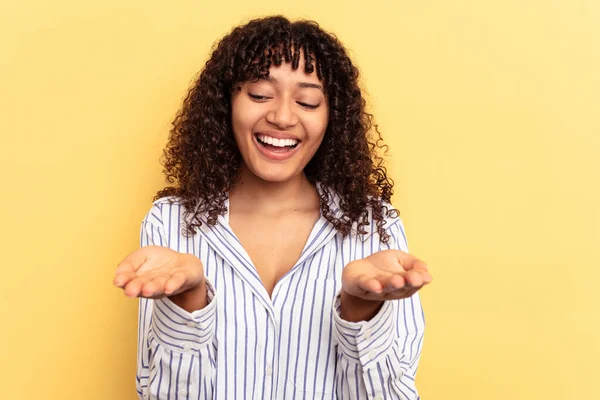 Sarı arka planda izole edilmiş genç bir ırk kadını elinde avuç içi bir şeyle kameraya sunuyor..