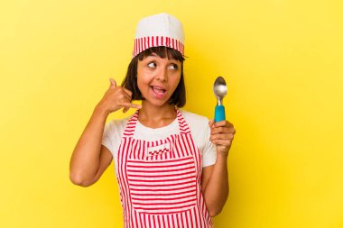 Sarı arka planda dondurmacı kadın dondurma tutuyor. Sarı arka planda izole edilmiş bir dondurma kepçesi tutan genç ırk dondurma üreticisi kadın. Cep telefonu hareketini parmaklarıyla gösteriyor..