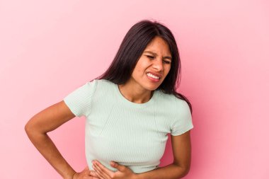 Pembe arka planda karaciğer ağrısı ve karın ağrısı çeken genç Latin bir kadın..