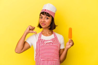 Sarı arka planda izole edilmiş dondurma tutan genç melez dondurma üreticisi kadın gururlu ve kendinden emin, örnek olarak.