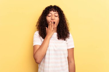Sarı arka planda soyutlanmış genç melez bir kadın esniyor. Ağzı eliyle kapatan yorgun bir jest yapıyor..