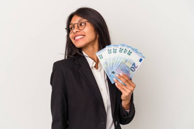 Beyaz arka planda izole edilmiş banknotları tutan genç Latin kadın gülümseyen, neşeli ve keyifli görünüyor..