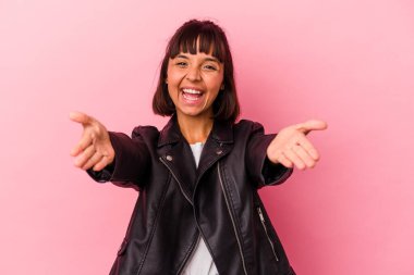 Pembe arka planda soyutlanmış genç melez bir kadın kameraya sarılıyor..