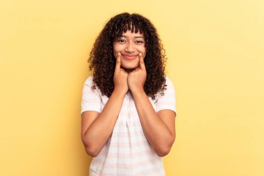 Genç melez kadın sarı arka planda izole edilmiş, iki seçenek arasında kuşkulanıyor..