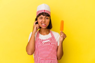 Dondurmacı kadın dondurma tutuyor. Sarı arka planda izole edilmiş. Kulakları elleriyle kapatıyor..