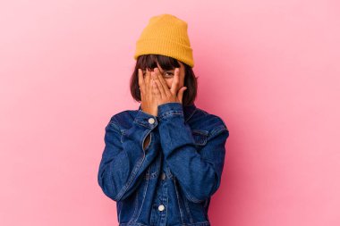 Genç melez kadın pembe arka planda izole edilmiş parmaklarıyla kameraya göz kırpıyor, yüzünü kapatmaktan utanıyor..