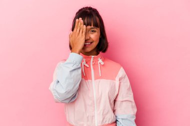 Pembe arka planda izole edilmiş genç melez kadın yüzünün yarısını avuç içiyle kaplayarak eğleniyor..