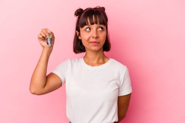 Genç melez bir kadın pembe arka planda izole edilmiş bir anahtar tutuyor. Amaçlarına ve amaçlarına ulaşma hayali kuruyor.