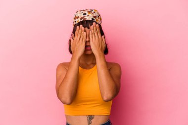 Pembe arka planda izole edilmiş genç melez kadın yüzünün yarısını avuç içiyle kaplayarak eğleniyor..