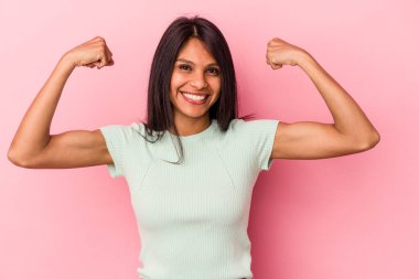 Pembe arka planda izole edilmiş genç Latin kadın güçlü bir hareket gösteriyor, kollarıyla, kadınsı gücün sembolü.