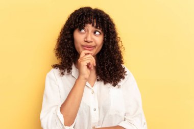 Sarı arka planda izole edilmiş genç melez kadın şüpheli ve şüpheci bir ifadeyle yana bakıyor..