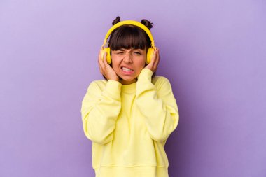 Mor arka planda kulakları elleriyle kapatan müzik dinleyen genç bir ırk kadını..