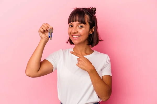 年轻的混血女子拿着一把钥匙 被粉色背景隔开 面带微笑地指着旁边 在空白的地方展示着什么 — 图库照片