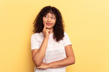 Genç melez kadın sarı arka planda izole edilmiş. Bir strateji planlıyor, bir iş yolu düşünüyor..