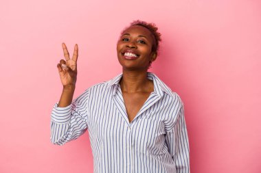 Genç Afrikalı Amerikalı kadın pembe arka planda izole edilmiş neşeli ve kaygısız parmaklarıyla barış sembolü gösteriyor..