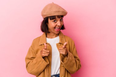 Pembe arka planda izole edilmiş genç melez kadın parmaklarıyla ön tarafı işaret ediyor..