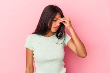 Pembe arka planda izole edilmiş genç Latin bir kadın. Başı ağrıyor, yüzüne dokunuyor..