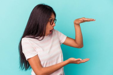 Mavi arka planda izole edilmiş genç Latin kadın elleri arasında bir kopya alanı tutarken şok ve hayrete düştü..