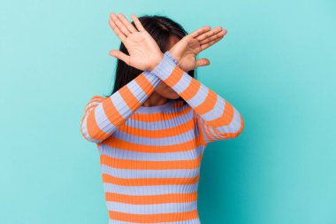 Mavi arka planda izole edilmiş genç Latin kadın iki kolu çapraz tutuyor, inkar kavramı.