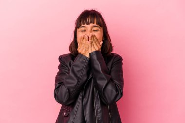 Pembe arka planda izole edilmiş genç bir ırk kadını bir şeye gülüyor, elleriyle ağzını kapatıyor..