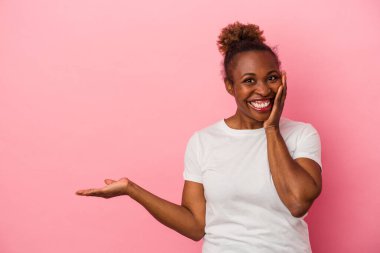 Pembe arka planda izole edilmiş genç Afrikalı Amerikalı kadın avuç içinde fotokopi alanı tutuyor, el üstünde tutuyor. Şaşırmış ve mutlu..