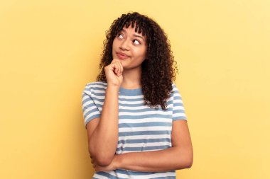 Sarı arka planda izole edilmiş genç melez kadın şüpheli ve şüpheci bir ifadeyle yana bakıyor..