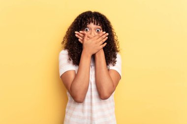 Sarı arka planda izole edilmiş genç bir ırk kadını elleriyle ağzını kapatırken şok oldu..