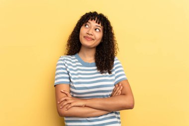 Sarı arka planda izole edilmiş genç melez kadın hedeflerine ve amaçlarına ulaşma hayali kuruyor.